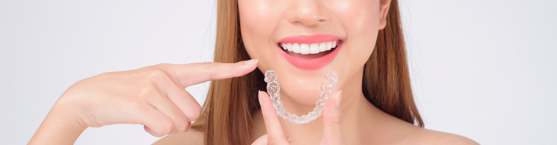 Woman holding clear aligner and pointing at smile.